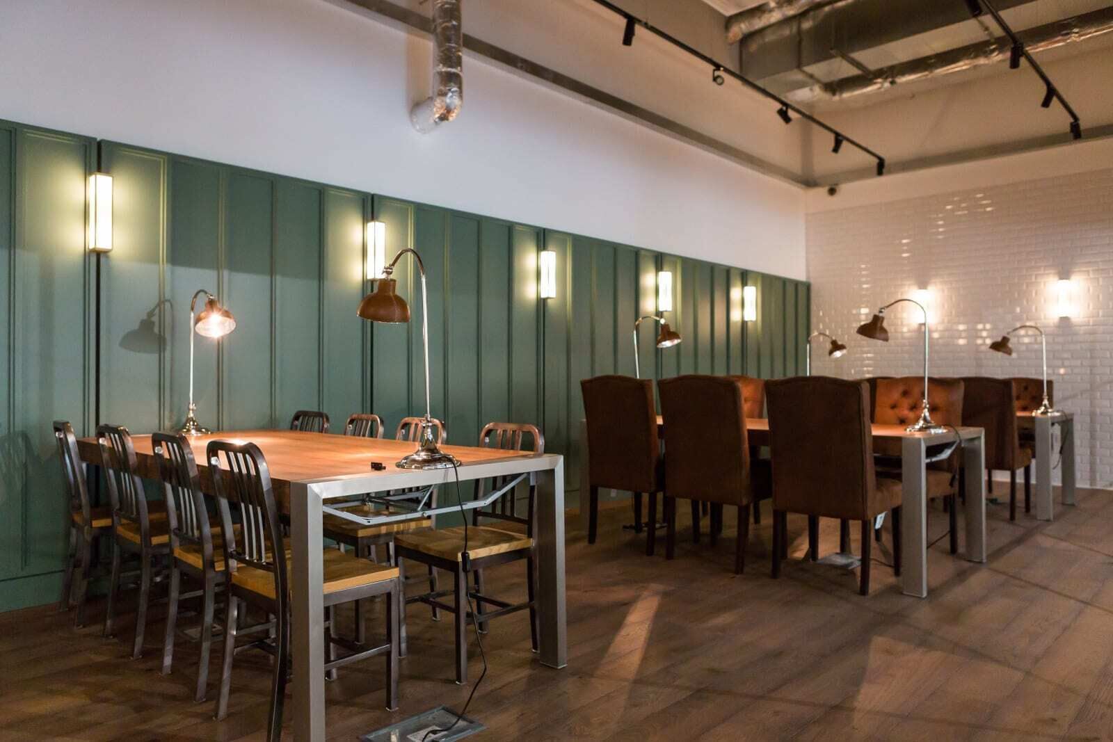Une salle de conférence avec une longue table et des chaises, des panneaux verts aux murs et des luminaires suspendus.