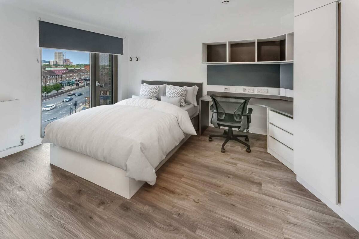 Ein modernes Schlafzimmer mit einem großen Bett, einem Schreibtisch und Blick auf eine Stadtstraße.