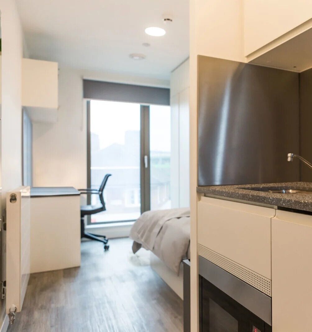 Een moderne hotelkamer met kitchenette, een bed, bureau en groot raam met uitzicht over de stad.