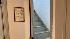Ein Korridor mit Holzboden, einer Tür, die zu einer Treppe führt, und einem gerahmten Bild an der Wand.