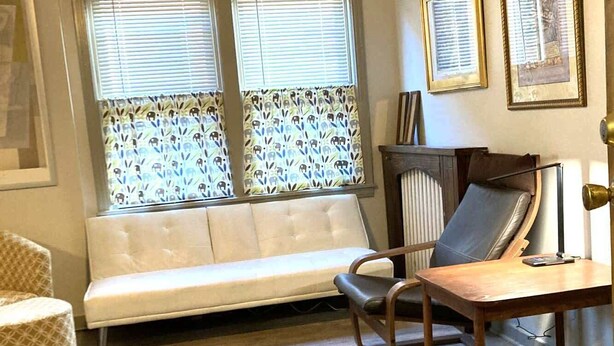 Ein Zimmer mit Deckenventilator, einer Couch, einem Sessel, einem Schreibtisch und einem Teppich.