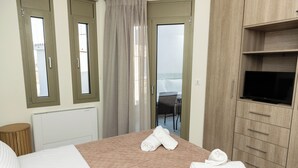 A hotel room with a bed, a TV, a wooden cabinet, and a view of the outdoors. - SeaSide Village (Dirfys-Messapia)