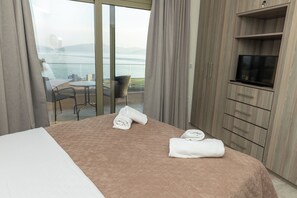 Une chambre d’hôtel avec un lit, une télévision, un balcon avec une table et des chaises, et une vue sur la mer.