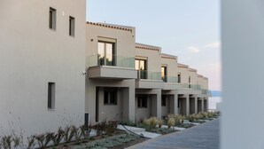 A modern hotel with a clean, minimalist design, featuring a row of balconies with glass railings and a paved walkway with landscaped gardens. - SeaSide Village (Dirfys-Messapia)