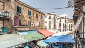 A narrow street with outdoor market stalls under umbrellas, old buildings with balconies, and air conditioning units. - La Casa sul Mercato by Wonderful Italy (Palermo)