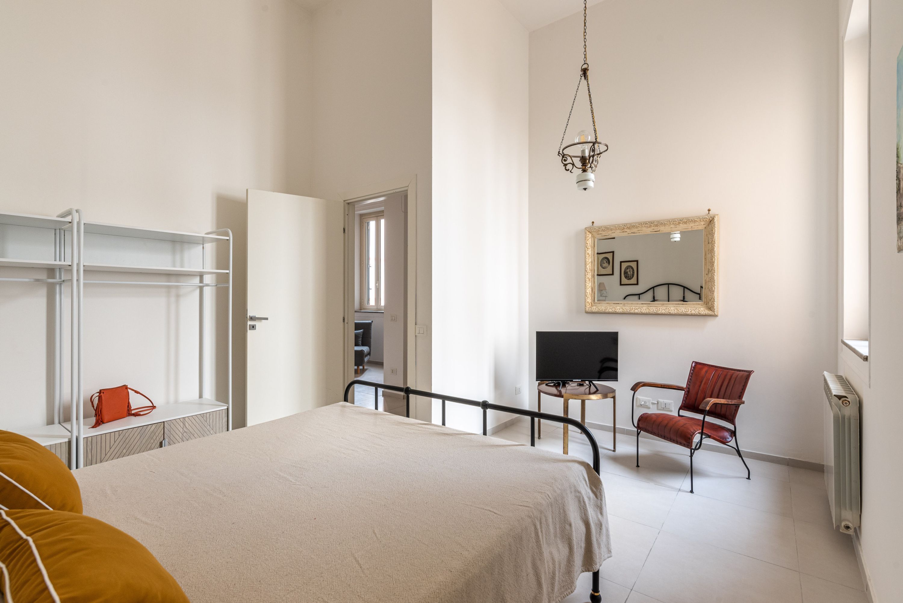 Une chambre à coucher avec un lit, une chaise, une télévision, une étagère et un miroir.