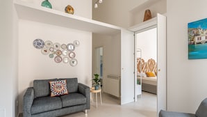 Un salon moderne avec un canapé gris, une petite table d’appoint ornée d’une plante et un mur décoré de différents motifs.