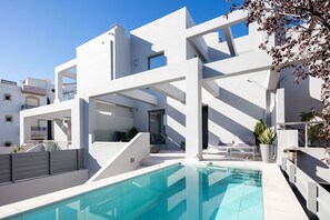 En moderne, hvid bygning med swimmingpool, udendørs siddepladser og en trappe til en øvre etage.