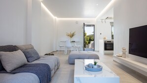 A modern living room with a sofa, ottoman, and coffee table, a dining area with chairs, and a kitchen with an oven and a TV. - Akonizia Luxury House - With Private Swimming Pool (Apokoronas)