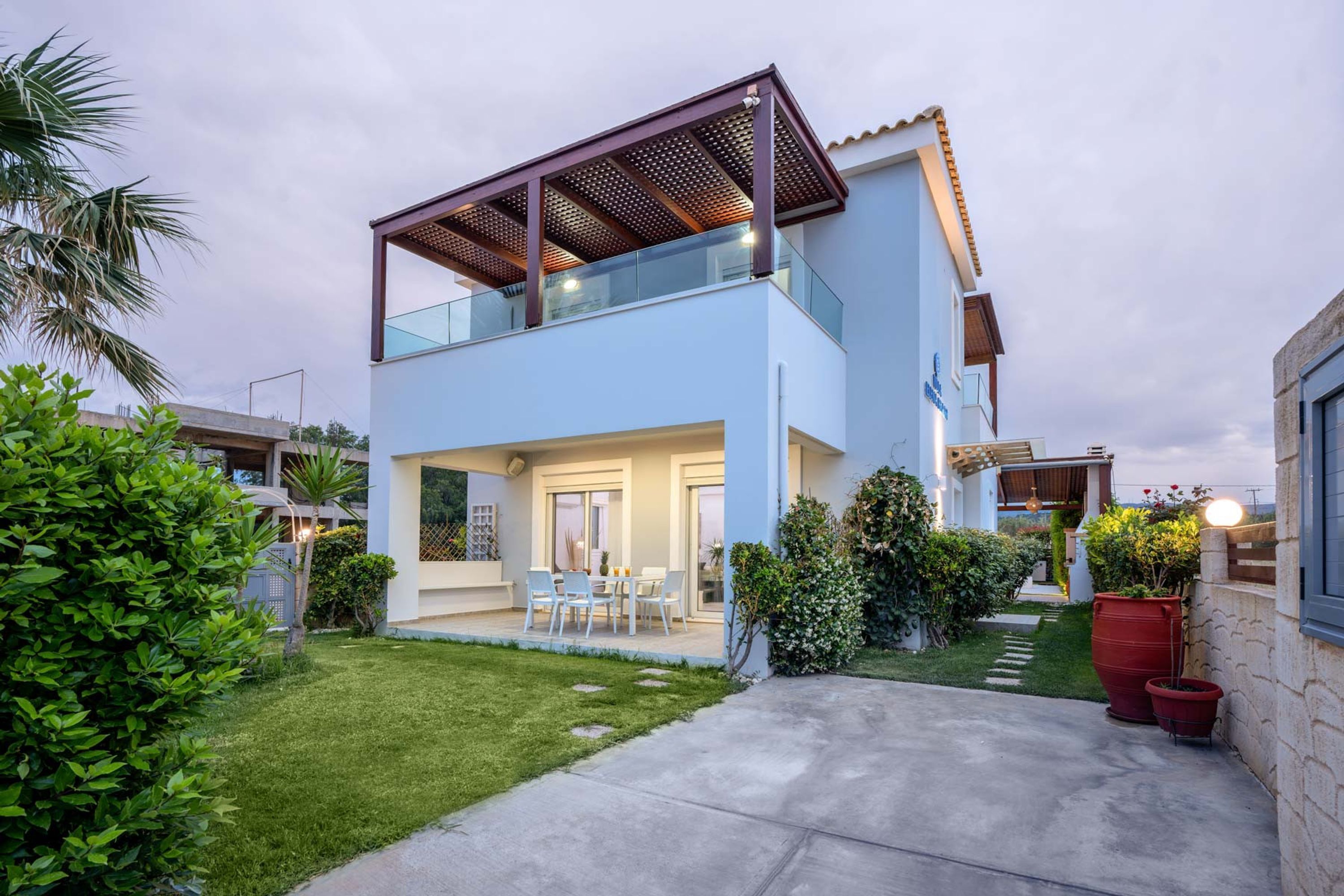 A modern two-story house with a balcony, a patio with outdoor furniture, and a well-maintained garden.