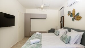 Moderni hotellihuone, jossa on suuri sänky, seinälle asennettu taulutelevisio, kattotuuletin ja koristeellinen taideteos seinällä.