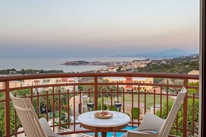 Un balcon avec une table et deux chaises, donnant sur une ville côtière et la mer.