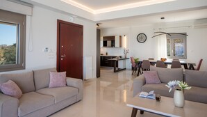 A modern living room with a sofa and coffee table, a dining area with chairs, and a kitchen in the background.