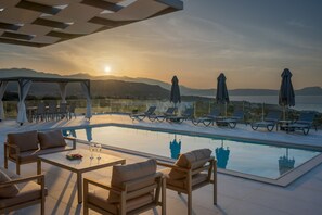 A poolside area with lounge chairs and a table, overlooking a body of water and mountains. - Villa Atyfia - With Private Pool (Rethymno)