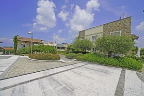 A residential area with a stone building, a paved courtyard, and surrounding greenery. - Residence Quadrivium 151 by Wonderful Italy (Castelnuovo del Garda)