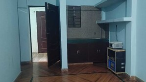 A narrow hallway with wooden flooring, a door leading to another room, and a kitchenette area with cabinets and a microwave. - Madhu Vatika Homestay By GRB (Patna)