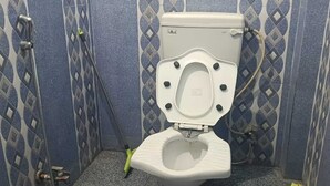 A toilet with a bidet attachment, a handheld showerhead, and a mop. - Madhu Vatika Homestay By GRB (Patna)