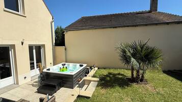 A backyard with a hot tub, a small palm tree, and a house with a tiled roof.