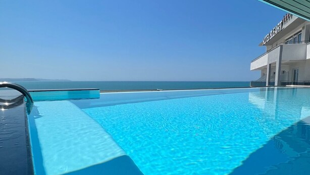 A clear blue pool with a view of the ocean and a hotel building in the background. - Luxury Rooftop Suites by Blumont (Rrashbull)