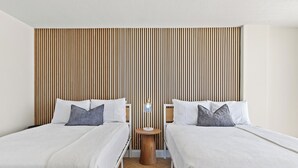Habitación de hotel con dos camas individuales, una mesita de noche redonda de madera con una lámpara y un cabecero de madera con listones.