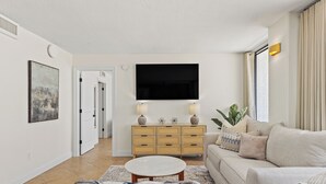 Una sala de estar moderna con un televisor de pantalla plana, un sofá color beige, un aparador de madera y una mesa de centro redonda.