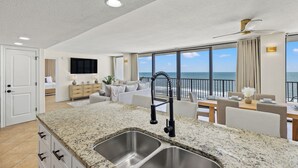 Una cocina moderna con encimeras de granito y fregaderos de acero inoxidable, un comedor con vistas al océano y un espacio de estar con un amplio ventanal con vista al mar.