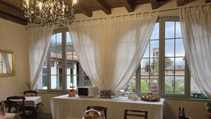 A dining area with a table set for four, a chandelier, and a view of the outside through large windows.