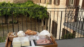 A balcony with a breakfast setup including croissants, cheese, and a coffee pot.