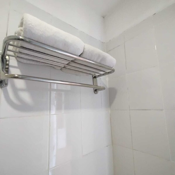 Un baño con paredes de azulejos blancos y un perchero metálico con dos toallas blancas.