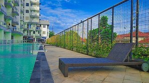 A poolside area with a lounge chair, a swimming pool, and a high-rise building in the background. - Dremzzz Vivo Jogja (Depok)