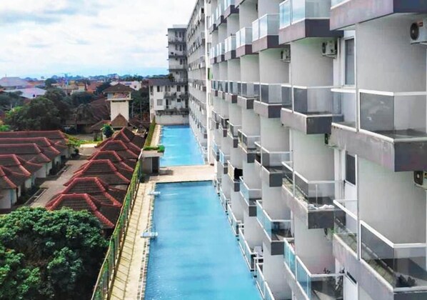 A modern hotel with a long swimming pool, multiple balconies, and a view of the surrounding neighborhood. - Dremzzz Vivo Jogja (Depok)