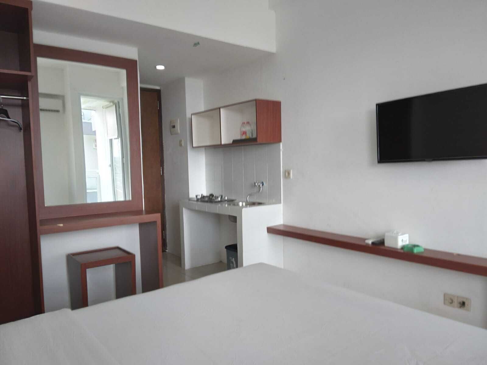 A hotel room with a bed, a small table, a mirror, a kitchenette, and a TV.