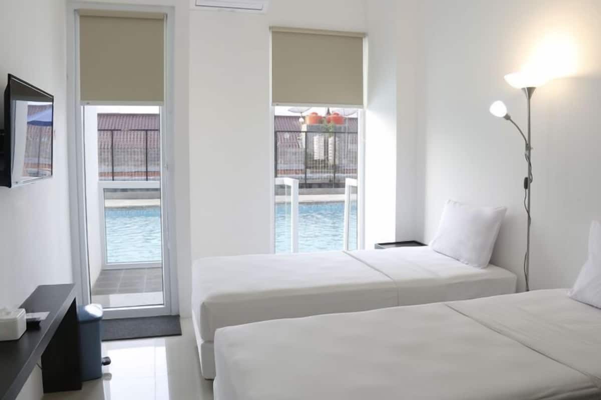 Ein Hotelzimmer mit zwei Betten, einem Schreibtisch, einem Sessel, einem Fernseher und Blick auf einen Pool.
