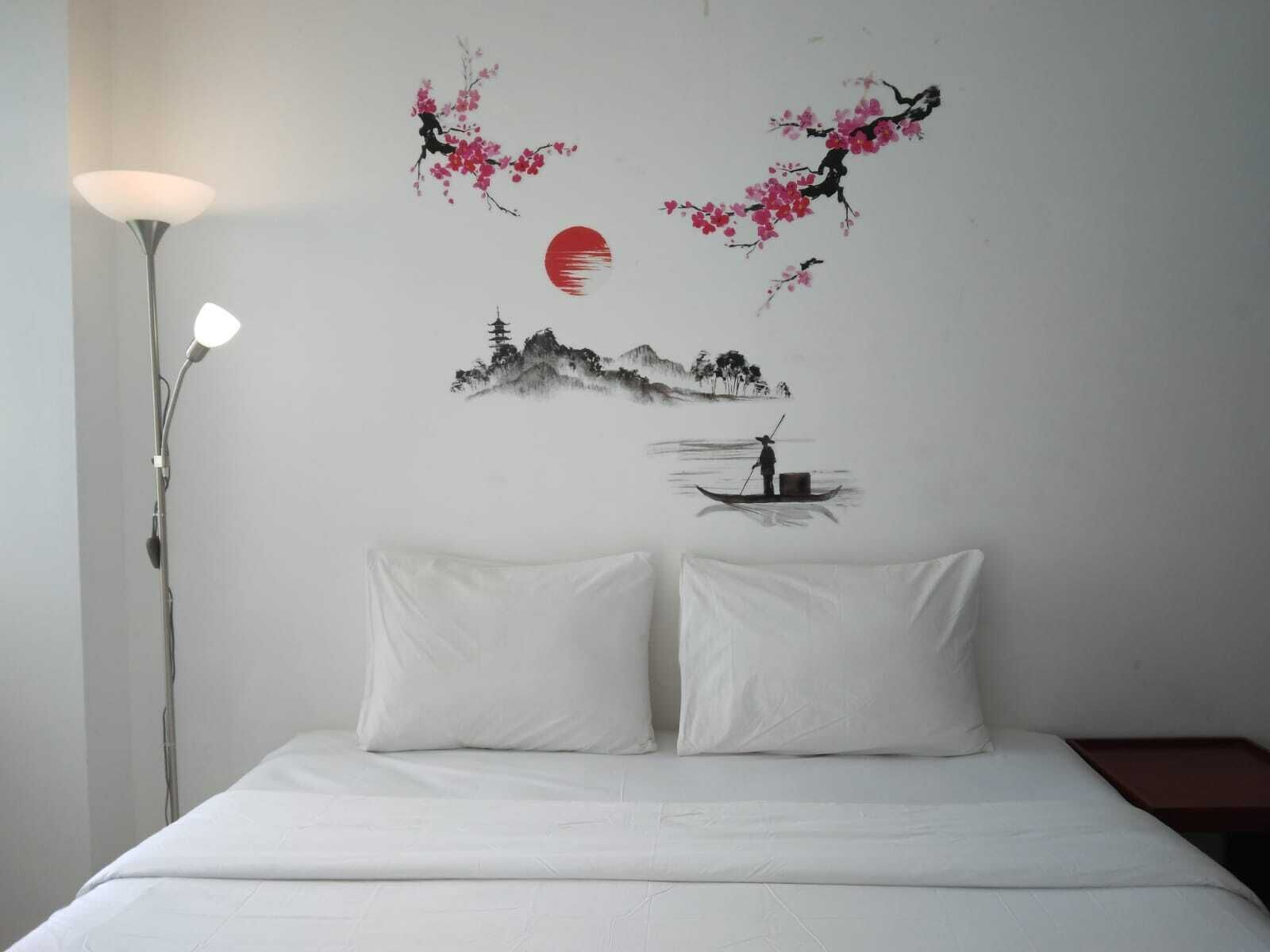 Una camera da letto con un letto, due cuscini, un comodino e una parete decorata con un dipinto raffigurante fiori di ciliegio, un sole e una montagna.