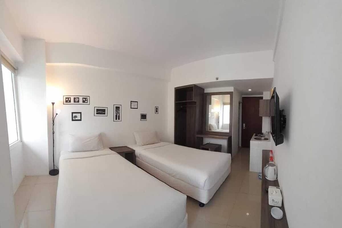 Ein Hotelzimmer mit zwei Betten, einem Schreibtisch, einem Spiegel, einem Fernseher und einer kleinen Küchenzeile.