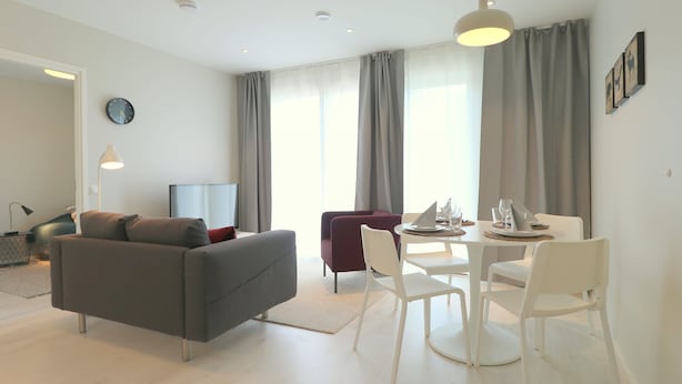 A modern living room with a grey sofa, a red armchair, a white dining table with chairs, and a large window with curtains. - Forenom Serviced Apartments Espoo Nupuri (Espoo)