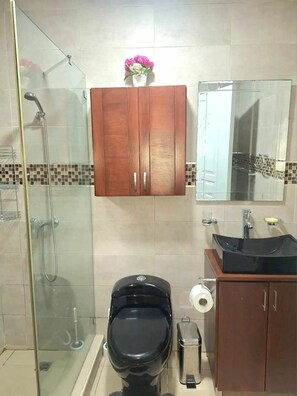 A bathroom with a glass-enclosed shower, a black toilet, a wooden cabinet, a sink with a black basin, and a mirror above the sink.