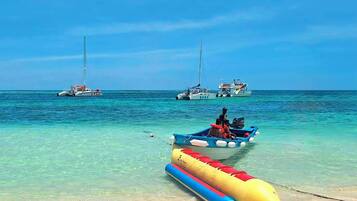 Una playa con agua turquesa cristalina, un bote inflable pequeño y dos botes más grandes a lo lejos.
