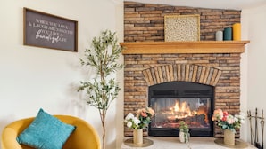 Una sala de estar con chimenea de piedra, un sillón amarillo y jarrones decorativos.