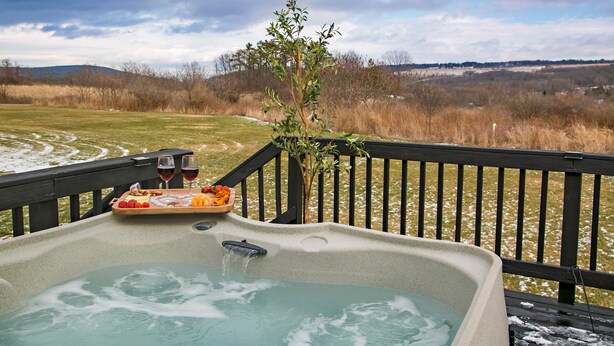 Un jacuzzi con terraza de madera, rodeado por un paisaje nevado y vistas a colinas distantes.