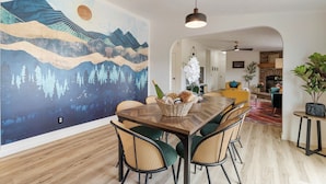 Un comedor con una mesa de madera, sillas de mimbre y un mural grande en la pared.