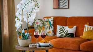 Un salón con un sofá, una mesa con una planta y dos copas de vino tinto, y un bol de aperitivos.