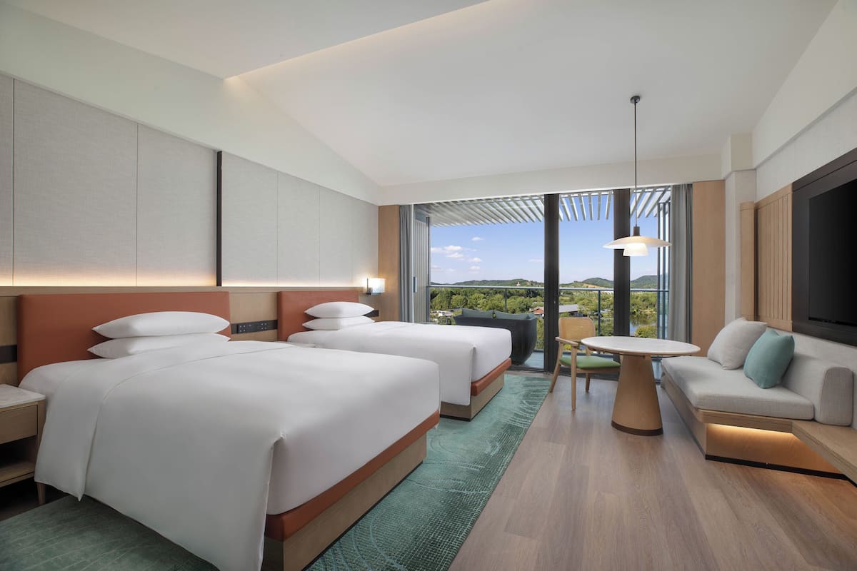 Une chambre d’hôtel moderne équipée de deux lits, d’un canapé, d’une table à manger et d’une grande fenêtre donnant sur l’extérieur.
