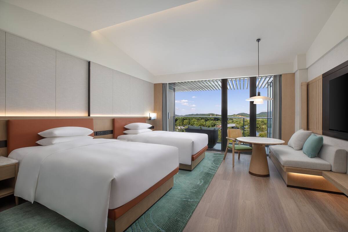 Une chambre d’hôtel moderne équipée de deux lits, d’un canapé, d’une table à manger et d’une grande fenêtre donnant sur l’extérieur.