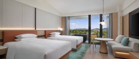 A modern hotel room with two beds, a sofa, a dining table, and a large window offering a view of the outdoors.