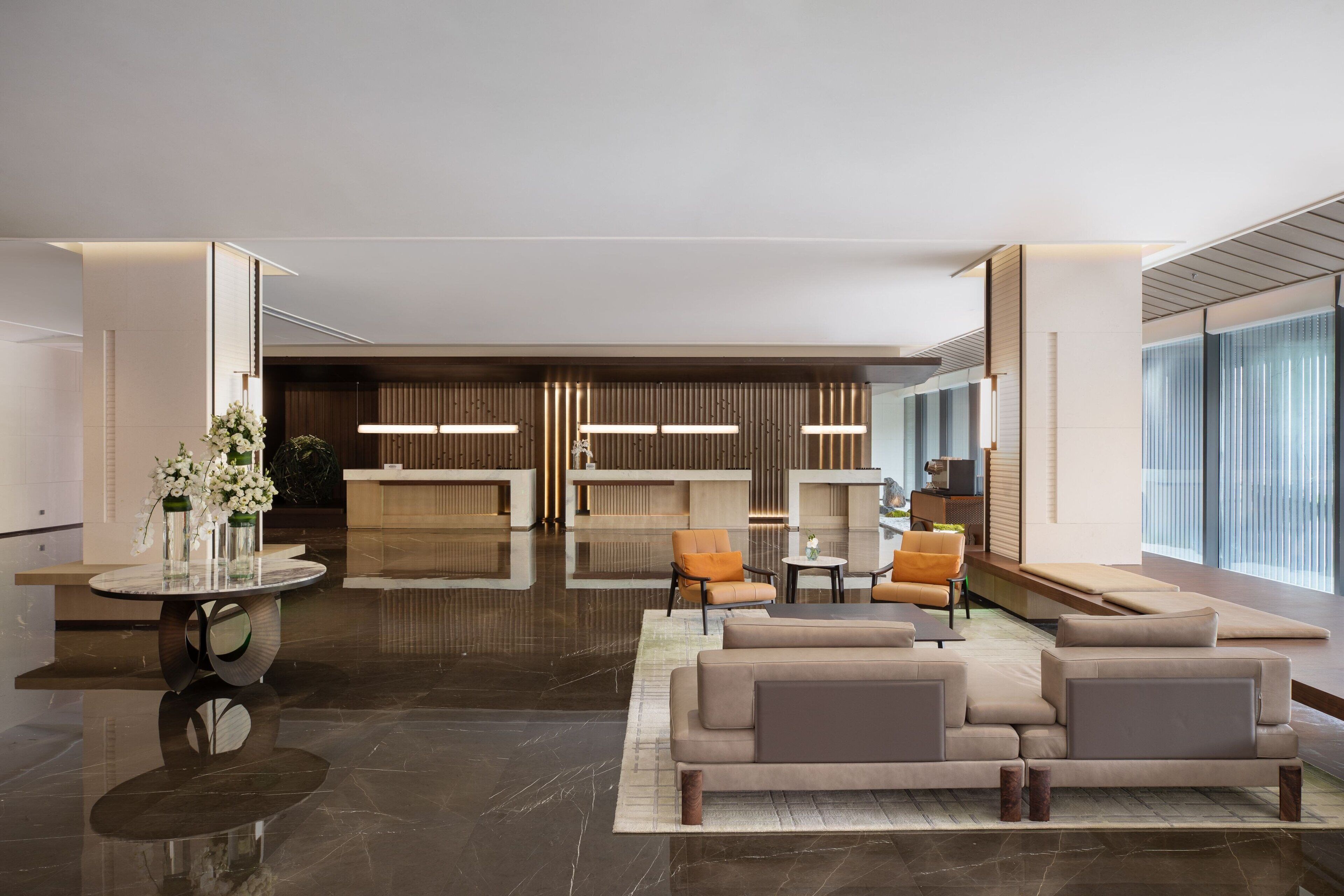 A modern lobby with a reception desk, seating area, and large windows.