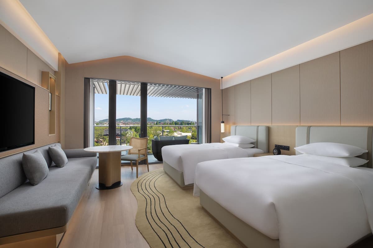 Une chambre d’hôtel moderne équipée d’un canapé, de deux lits, d’une télévision, d’une table et offrant une vue sur la ville.