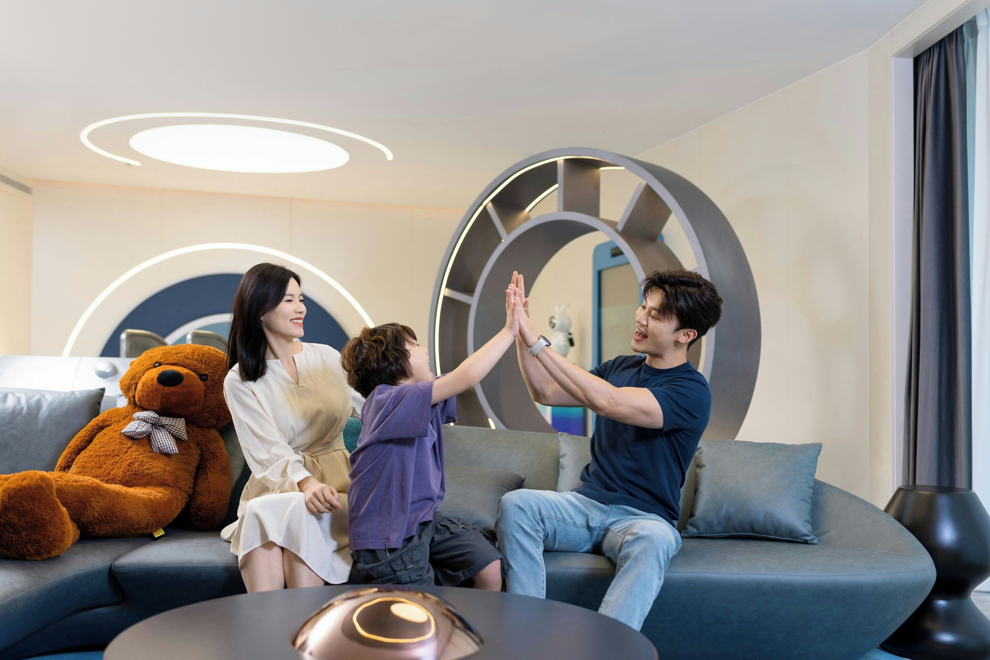 A modern living room with a sofa, a large teddy bear, and a coffee table.