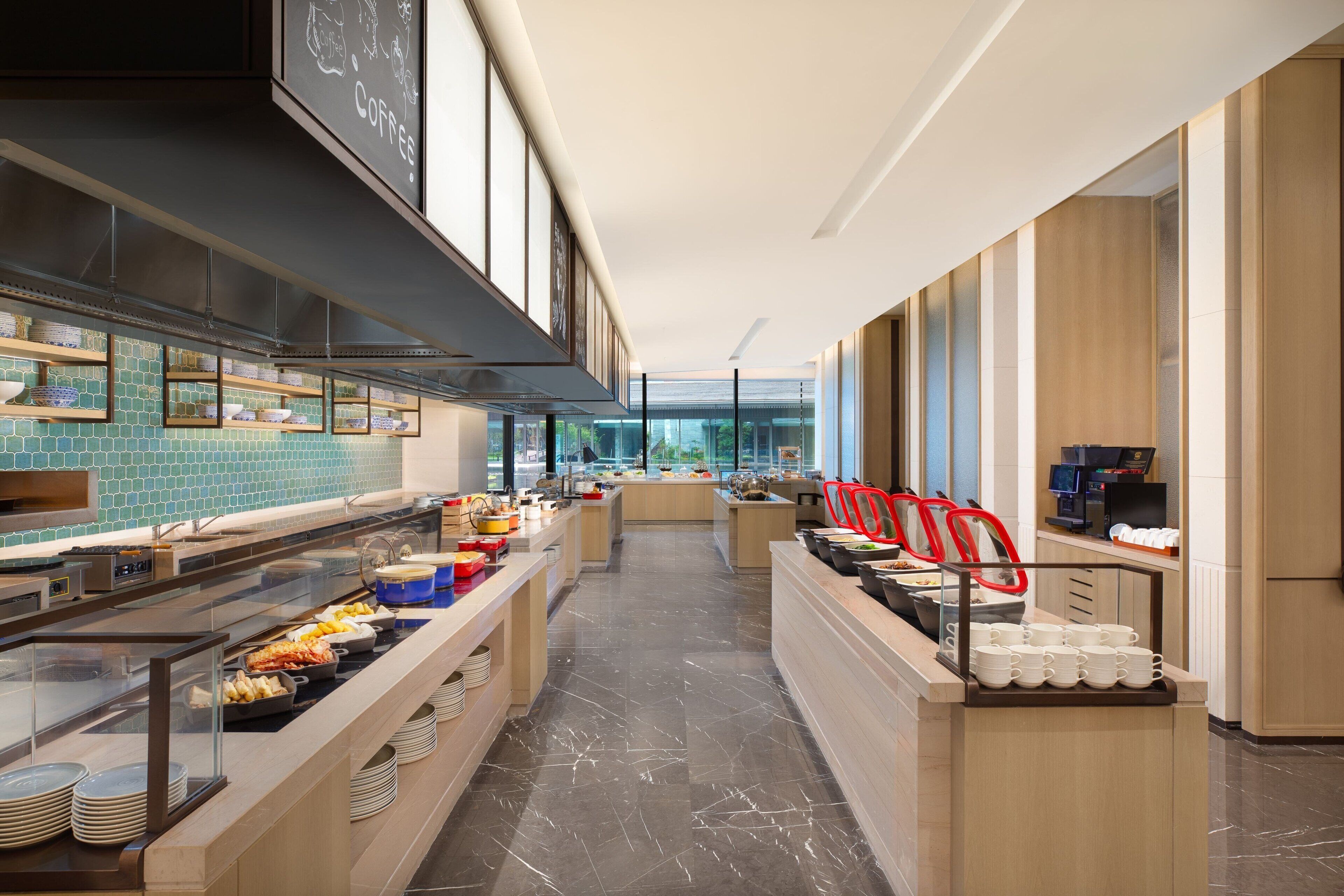 A modern buffet setup with various food stations, a long counter, and a clear view of the kitchen area.