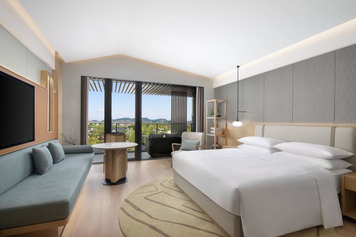 Une chambre d’hôtel moderne dotée d’un grand lit, d’un canapé, d’une télévision et d’un balcon avec vue.